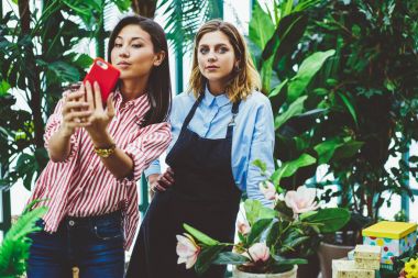 Neşeli Asyalı kadın smartphone makinesinde orangery sahibi ile paylaşım ağlarında, meslektaşları greenhous çalışma işlemi sırasında cep telefonu uygulaması üzerinde fotoğraf çekimi için selfie yapma