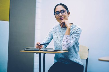 Genç kadın notlar proje öğrenme sınıf derslerinde, planlama için bilgi analiz masada oturan ev ödevi görev yaparken durulması Eyewear düşünceli zeki kız öğrenci