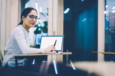 Notlar, Danışma, yetenekli kız öğrenci dizüstü bilgisayar ile boş ekran üzerine ders kullanarak rapor yazma kamera bakarak oturmak üniversite sınavına hazırlanıyor ciddi genç kadın portresi