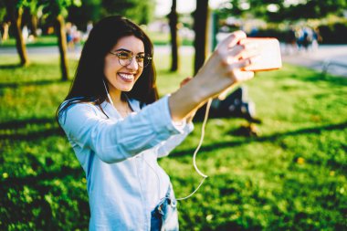 Mutlu kız öğrenci selfie smartphone kameraya yapmak için poz rekreasyon ile paylaşım ağlarında için güneşli Park dinlenme sırasında resim yolu ile hareket eden alarak neşeli hippi kız memnun.