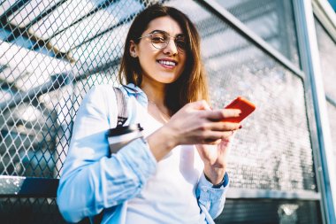 Gözlük bloglama sosyal ağlar açık havada serbest zaman sahip kız öğrenci gülümseyen, neşeli genç kadın manifatura mesaj mobil arkadaşlarınızla sohbet üzerinde sokakta duran tarifeler ile memnun