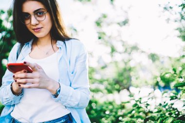 İleti gönderme ve smartphone reklam için kopya alanı üzerinde duran yüklemek için mobil uygulama kullanan hipster kız sohbet bahar gününde açık havada dinlenme rahat kıyafet genç kadın