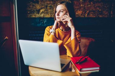 Düşünceli işkadını uzaktan kafede dizüstü bilgisayarda çalışan pencereden dışarı bakarak telefon görüşme sırasında eserin problem çözme. Dalgın sahibi Smartphone'da konuşuyor