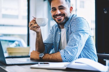 Ağ dizüstü bilgisayarda kahve, yetenekli gülümseyen freelancer holding Kupası online iş projesi başarıyla tamamladıktan sonra içme sırasında mola zevk neşeli erkek öğrenci portresi