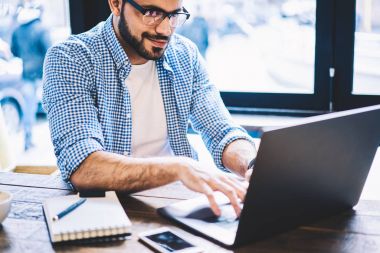Bilgi ağları üzerinden arama netbook klavye olumlu hipster adam kafede otururken online para kazanmak uzak iş dizüstü bilgisayarda yazarak yetenekli erkek serbest meslek