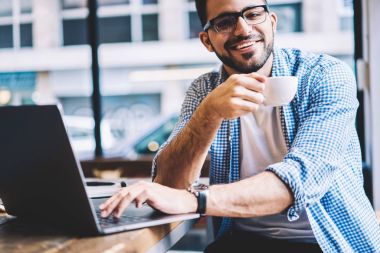 Zengin erkek portresi bu netbook, başarılı freelancer Kupası ve bloglama ağlarda tutan kamera bakarak web sayfasında dosya indirmeyi kafede kahve aroması tadını geliştirici