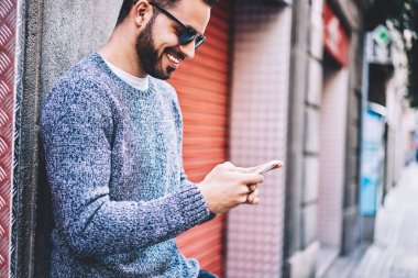 Neşeli hipster adam komik video web sitesi Caddesi üzerinde duran, genç adam kısa mesaj sohbet arkadaş gülümseyen smartphone üzerinden izlerken geri bildirim gönderme online istimal telefon kullanma