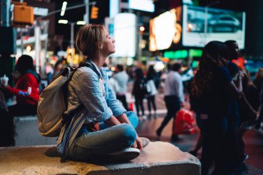 Sosyal ağlar üzerinden cep telefonu ve internet bağlantısı gezi New York'ta gece, kadın seyahat blogging, Simgesel Yapı üzerinden fotoğraf göndererek smartphone ile Times Meydanı'nda oturan hippi kız