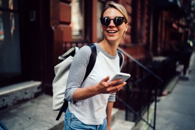 Mutlu genç kadın zaman açık havada sohbet, neşeli hippi kız sokak arayan uzak tutan cep telefonu elinde yürüyüş gülüyor için smartphone tutan harcama hafta sonları zevk güneş gözlüğü