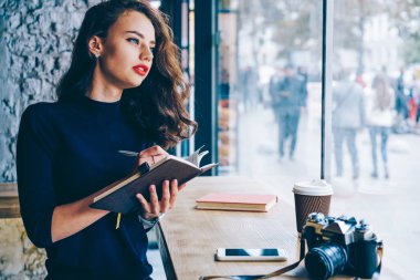 Pencereden dışarı bakarak ve Not Defteri ile vintage fotoğraf makinesi ve lezzetli içecek rekreasyon vaktinizi kafede oturan metin bilgileri yazarak düşünceli yetenekli öğrencisi. Kopyalama alanı alanı