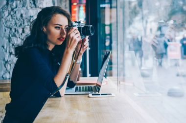 Ahşap masa kahve dükkanında kablosuz yüksek hızlı 4 g bağlanan dizüstü bilgisayar ile oturup kendi web sitesinde yayımlanması için vintage fotoğraf makinesi fotoğraf yapma profesyonel genç fotoğrafçı Internet