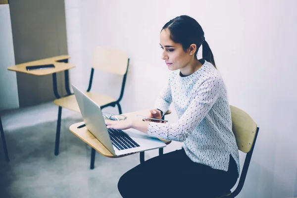 严肃的妇女学习使用膝上型计算机应用程序阅读信息从网页坐在教室里 女学生浏览上网本规划课程项目使用技术 — 图库照片