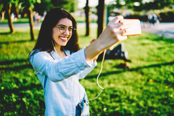 快乐的女学生摆姿势 使自拍的智能手机相机满意的娱乐 开朗的时髦女孩拍照通过移动期间在公园休息 在阳光明媚的日子里分享网络 — 图库照片
