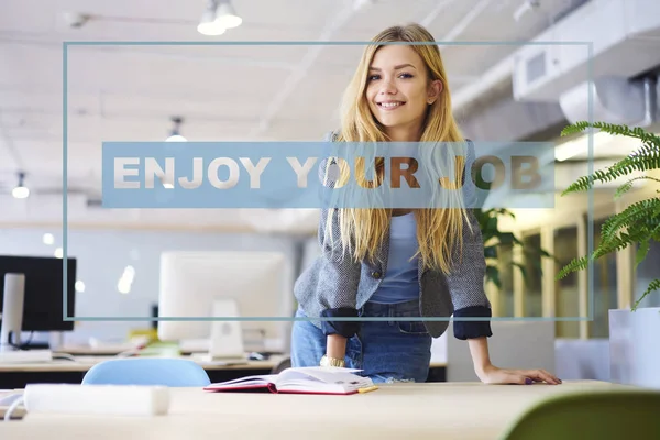 Half length portrait of positive caucasian female employee enjoying her job in coworking office. Cheerful young creative worker with blonde hair smiling at camera office, infographic conceptual idea