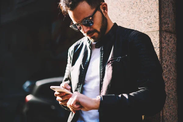 物思いにふける若者のウェブサイトで最新のニュースを読みながら時間をチェック 腕時計を見て 電話屋外経由でテキスト メッセージを送信する会議を待っている流行に敏感な男のスマート フォンで閲覧 — ストック写真