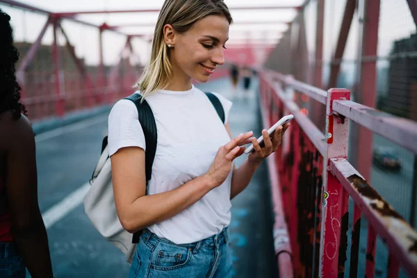 橋の上を歩いてのスマート フォンを介してチャット内気な少女の笑みを浮かべて女性旅行週末旅行中に通信のローミングでインターネット接続を使用して都市の設定の近くに立ってを正 — ストック写真