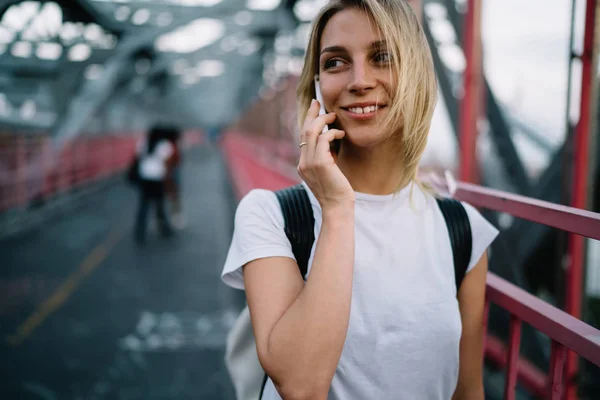 Smiling young woman in t-shirt with copy space for label or brand name talking on mobile phone walking,hipster girl satisfied with tariffs for making calls in roaming having telephone conversatio
