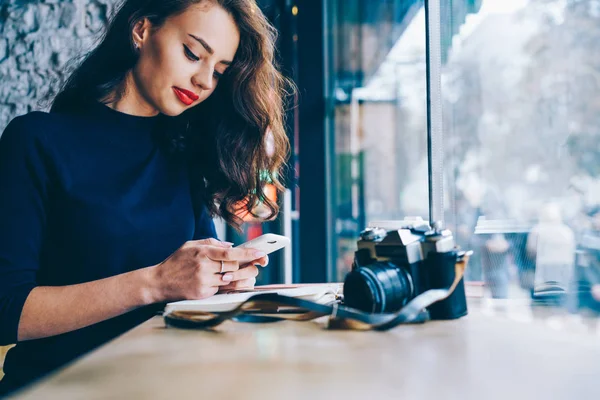 美しい若い女性の Wifi ゾーンでコーヒー ショップ インテリア ビンテージ カメラでテーブルに座っている現代の携帯電話で 同僚とのオンライン チャットします 広告テキスト — ストック写真