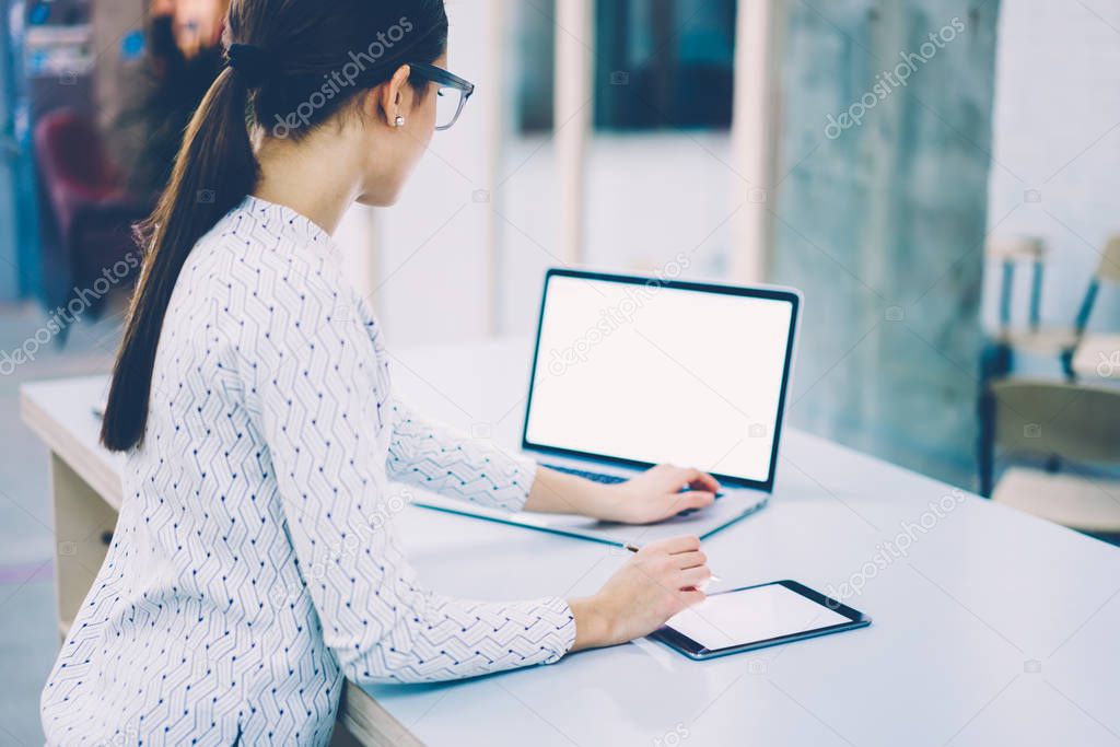 Skilled female web designer using modern device with mock up screen for drawing illustration online,woman signing documentation on digital tablet synchronizing multimedia file with laptop computer