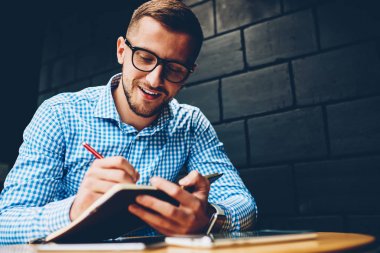 Gözlük yaratıcı erkek Tasarımcısı grafik kafe, pozitif öğrenci kampüs içinde öğrenme Not Defteri'nde fikirler yazma ödev görevleri yerine getirmeye çalışan sketchbook projede planlama yapmaya konsantre