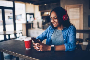 Neşeli afro Amerikan hippi kız müzik dinleme online arkadaş ile iletişim modern kırmızı kulaklık. Kahve molası bloglama ağlar üzerinden cep zevk öğrenci mutlu koyu derili