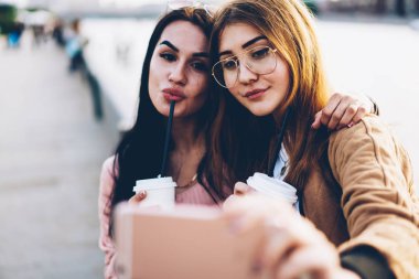 Görüntü lezzetli kahve ön kamera dijital hareket eden telefon aygıt üzerinde seyir ve kentsel ortamda dostu toplantı sırasında fotoğraf çekmek elinde olan çekici gülümseyen genç kadın kapatmak