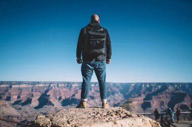 Yüksek rock doğa manzara, Büyük Kanyon ABD'deki vahşi ortamda sırt çantası ile hiking dağın tepesine ulaşan erkek Gezgin gözlemleyerek cliff üzerinde duran sırt çantası ile Arkadan Görünüm adam avare