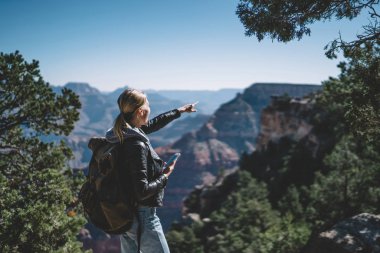 Uygulama sırasında ABD, smartphone elinde tutan yüksek dağda işaret hippi kız vahşi doğa keşfetmek yol yön kontrol etmek için pozitif kadın seyahat etmek sırt çantası ile memnun