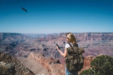 Genç hippi kız okuma mesajı smartphone ayakta dağlar bakış açısı gezici, kadın turist tur sırasında iletişim kurmak için doğada iyi mobil veri bağlantısı kullanarak sırt çantası ile kullanma