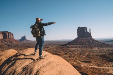 Arkadan görünüşü erkek traveler ABD ayakta yüksek tepede, sırt çantası duygu özgürlük Monument Valley oluşumunda scenerysandstone bakarak kaya üzerine adamla hipster başarılı yolculuk kutluyor