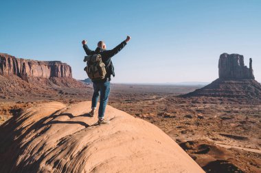 Arkadan görünüşü erkek traveler ABD ayakta yüksek tepede, sırt çantası duygu özgürlük Monument Valley oluşumunda scenerysandstone bakarak kaya üzerine adamla hipster başarılı yolculuk kutluyor
