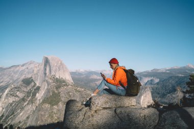 Mobil Mesaj, vahşi natur keşfetmek telefon aracılığıyla posta göndermek için iyi telefon bağlantısı olan kadın seyahat tur hiking sırasında dinlenme yüksek kayaların üzerinde oturan kullanan genç kadın