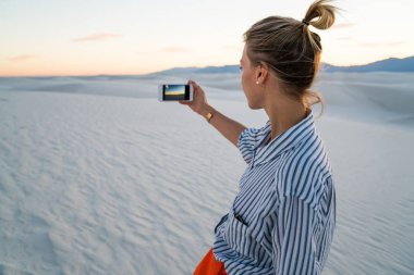 Hippi kız cep telefonu ünlü Amerikan dönüm noktası beyaz ziyaret resim yapma tutan kumları Park batımında, arkadan görünüşü doğal Doğa manzara fotoğraflarını smartphone kamera çekimi kullanan genç kadın