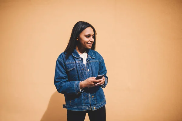 微笑的美国黑人女性牛仔裤夹克站在宣传背景下 发送信息聊天在社交网络 时髦的穿着时髦的女孩检查电子邮件框站在宣传区 — 图库照片