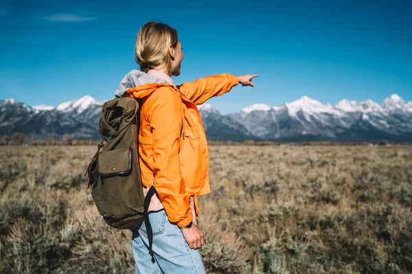 年轻的女性游客在她的面前展示美丽的风景 享受发现野生自然 时髦女孩与背包指向雪山到那里在徒步旅行流浪旅行 — 图库照片