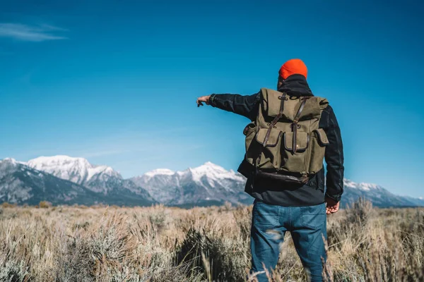 后面的男性旅行者与背包指向山顶计划到达在徒步旅行期间 时髦的家伙流浪显示高降雪峰远离探索美丽的美国自然 — 图库照片