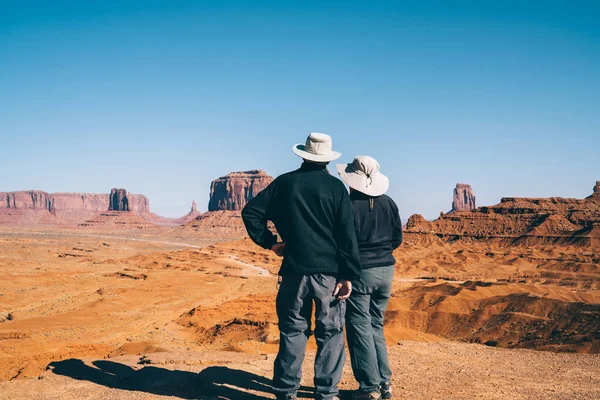 Back view of male and female american tourists observing beautiful landscape of Monument valley,couple of travelers enjoying excursion to famous american landmark together looking at stone formatio