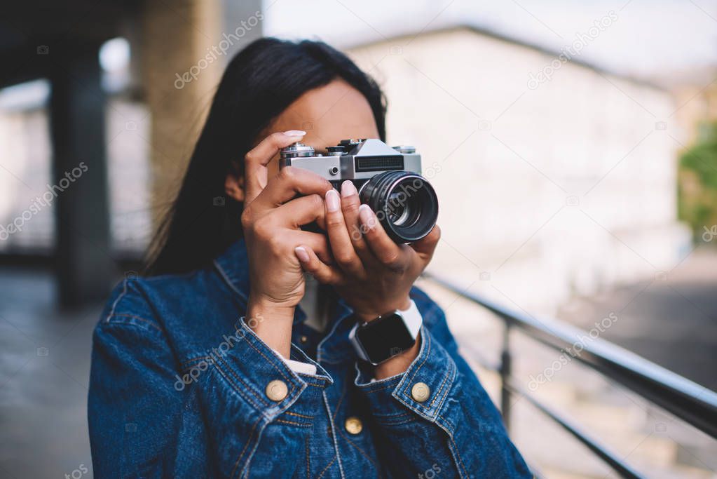 Young dark skinned hipster girl in jeans jacket spending time on hobby taking pictures on city street while resting on weekends,afro american tourist making photos during leisure strolling outdoors