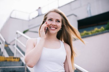 Uluslararası telefon görüşmesinde gülen neşeli beyaz kadın şehrin boş zamanlarının tadını çıkarıyor. Uygulama yoluyla gezen interneti mobil iletişim için kullanan mutlu kadın.
