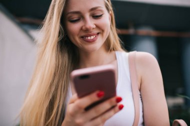Çevrimiçi akıllı telefon oyunlarının mutlu kadın test edicisi yeni alınan uygulamaları kontrol ediyor açık havada kendini iyi hissediyor, neşeli beyaz blogcu web yayını için metin içeriği yazıyor 4G kablosuz