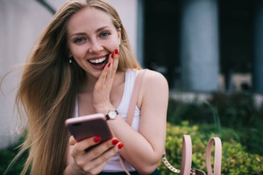 Heyecanlı neşeli web blogcusunun portresi açık havada cep telefonu zımbırtısında hesap bakiyesinin şokunu hissediyor, akıllı telefon bağlanma olanaklarından etkilenen pozitif kadın