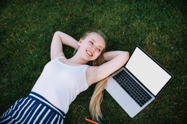Neşeli kadın dijital göçebenin yaz çimlerinde uzanması ve kendi yaşam tarzının tadını çıkarması, uzak işi, reklam metni için boş ekran alanı olan modern dizüstü bilgisayar veya web siteniz.