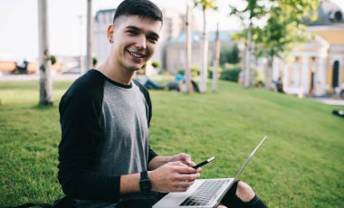 Milenyum çağındaki gündelik hipster bir adamın portresi dijital cep telefonunu elinde tutuyor ve boş zamanlarında dizüstü bilgisayarın güncellenmesini bekliyor. Modern teknolojileri kullanan pozitif erkek serbest yazar.