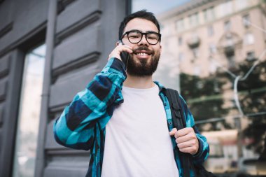 Neşeli Kazak erkek turistin yarım boy portresi şehir ortamında durup kameraya gülümserken uluslararası aramanın keyfini çıkarırken en iyi arkadaşının 4 g internete bağlanıp gezintiye çıkması.