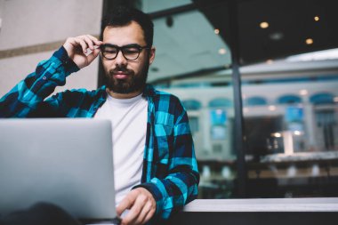 Konsantre erkek grafik tasarımcısı iş başvurusunu serbest çalışan dizüstü bilgisayarda kullanıyor, göz giyimi uzmanı modern netbook üzerinden netbook üzerinden ağlardan dosya indiriyor.