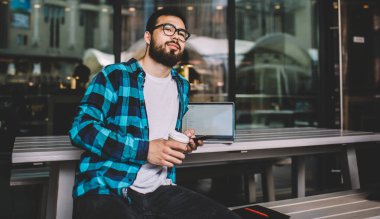 Kazak genç adam elinde kahve olan akıllı telefondan gelen mesajın üzerine kafa yoruyor. Optik gözlüklü yakışıklı hippi sokak kafeteryasında cep telefonunu kullanarak göz koruması sağlıyor.