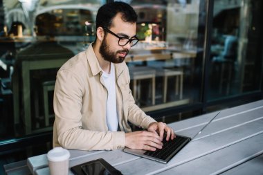 Modern bilgisayar yükleme uygulamasında optik göz giyimi klavyesinde kablosuz internet bağlantısı kullanan yetenekli erkek serbest yazar, yeni web sitesi için tasarımla çalışan dizüstü bilgisayarda yazı yazar