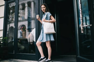 Çekici bir genç kızın kafeteryadan kafein bardağıyla çıkan ve kameraya bakan, marka ya da etiket için fotokopi alanı olan bir kadın portresi.