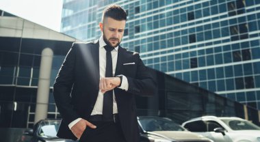 Finansal bölgedeki kurumsal girişimde buluşmadan önce kol saatini kontrol eden, giyilebilir aksesuar kullanan ciddi bir erkek girişimcinin gözünün önünde.