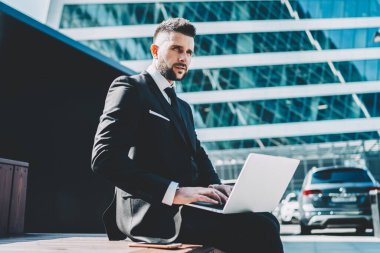 Düşünceli erkek tüccar şehir merkezinde açık havada oturarak online iş ile ilgili sorunu çözerken, girişimci bilgisayardan dosya yüklemeyi düşünerek kapandı